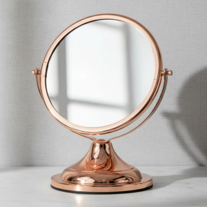 Espelho de aumento para maquiagem, redondo dupla-face, de mesa com acabamento em Red Gold, sobre bancada de mármore com fundo cinza.