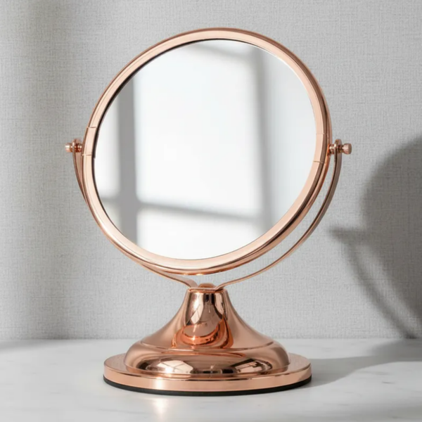 Espelho de aumento para maquiagem, redondo dupla-face, de mesa com acabamento em Red Gold, sobre bancada de mármore com fundo cinza.