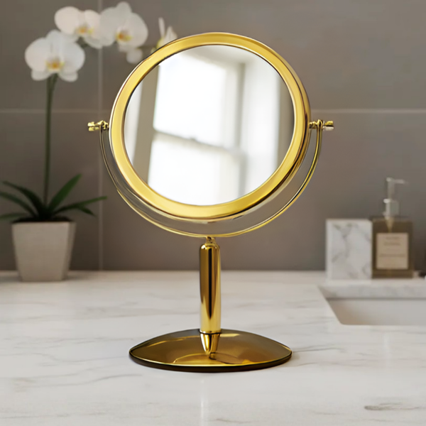 Espelho de aumento para maquiagem, redondo, de mesa, acabamento gold, sobre bancada de banheiro, foco no design metálico e na superfície refletiva.