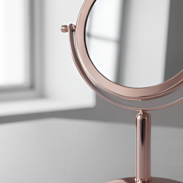 Espelho de aumento para maquiagem, redondo, de mesa, acabamento rose gold, em ambiente interno iluminado, foco no detalhe da moldura metálica.