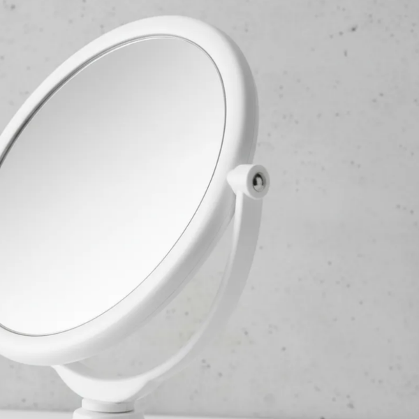 Espelho de aumento para maquiagem, redondo, de mesa, acabamento branco, em ambiente de banheiro, com foco na lateral do espelho.