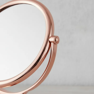 Espelho de aumento para maquiagem, redondo com acabamento Red Gold, de mesa com foco no aro ajustável, em fundo cinza.