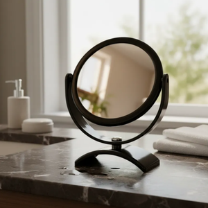 Espelho de aumento para maquiagem, redondo, de mesa, acabamento preto, sobre bancada de banheiro, foco no espelho e na base.