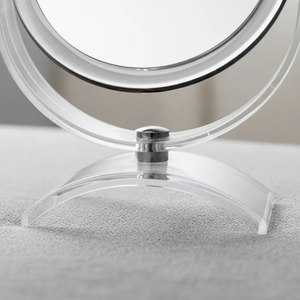 Espelho de aumento para maquiagem, redondo, de mesa, acabamento cristal, em superfície neutra, foco na base curva.