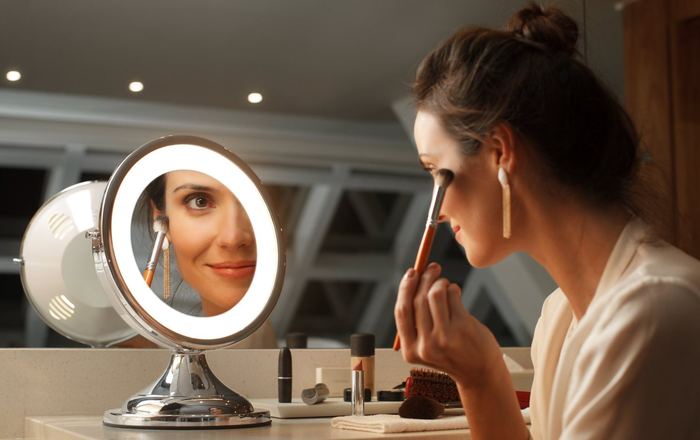 Espelho Gardie com LED aceso refletindo o rosto de uma mulher durante a maquiagem